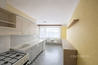 Kuchyně s linoleem a velkým oknem, světlé skříňky, prostorný jídelní kout, žluté stěny vytvářejí moderní a útulný prostor.