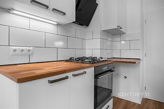 Moderní kuchyň s dřevěnou pracovní deskou, bílými lesklými skříňkami a vestavěnou troubou. Dlaždice na stěně zvyšují estetický dojem.