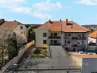 Exteriér rodinného domu s plochou střechou, balkony a předzahrádkou, nacházející se v klidné rezidenční čtvrti.
