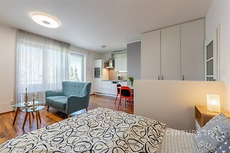 Moderní obývací pokoj s kuchyňským koutem, parketová podlaha, velká okna, světlý interiér, vestavěné skříně, elegantní nábytek.