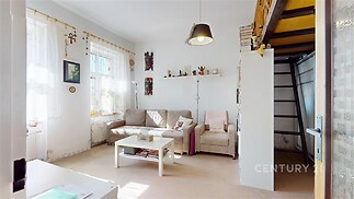 Světlý obývací pokoj s parketovou podlahou, velkými okny a moderním nábytkem, nabízí pohodlné posezení a útulnou atmosféru pro relaxaci.