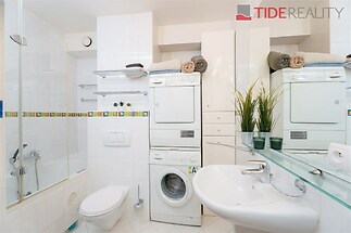 Koupelna s bílými dlaždicemi, vestavěnou skříní a moderní sanitou, obsahující pračku a sušičku pro praktické využití prostoru.