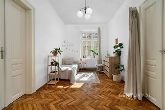 Světlá ložnice, parketová podlaha, velká okna, moderní interiér, rostliny a dekorativní prvky, klidná atmosféra, ideální pro relaxaci.