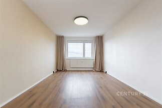 Prostorná ložnice s parketovou podlahou, velké okno poskytující dostatek světla, moderní minimalistický styl interiéru.