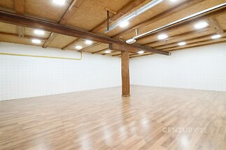 Prostorný otevřený prostor s dřevěnou parketovou podlahou, viditelnými trámy a bílými dlaždičkovými stěnami, nabízí moderní a světlý interiér.