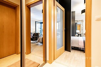 Vstupní hala s dřevěnou parketovou podlahou, zrcadlovými dveřmi a moderním osvětlením, vedoucí do světlého obývacího pokoje.