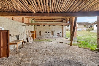 Zastřešený venkovní prostor s dřevěným stropem a kamennou zdí, ideální pro rekonstrukci. Přístup na zahradu, přírodní prvky, rustikální styl.