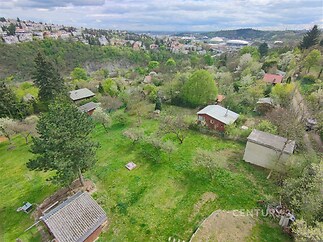 Přírodní pozemek s výhledem na krajinu, obklopen stromy a keři, v klidné lokalitě s rekreačními chatami a zelení, ideální pro milovníky přírody.