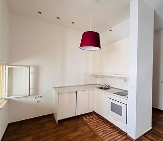 Světlá kuchyň s dřevěnou podlahou, moderními bílými skříňkami a stylovým červeným osvětlením, ideální pro útulné bydlení