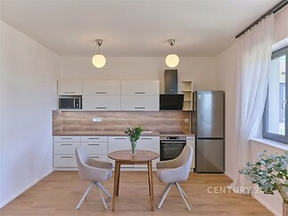 Moderní kuchyň s dřevěnou podlahou, světlým nábytkem a velkými okny, elegantní povrchová úprava, prostorný design, vynikající světelnost.