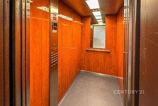 Výtahem obložený dřevěným dekorem, moderní design s kovovými prvky, zrcadlem a kombinovaným osvětlením pro světlý interiér.