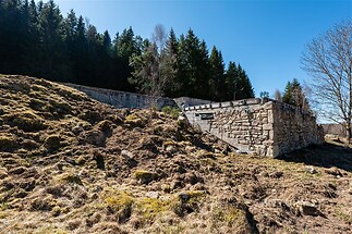 Kamenná opěrná zeď obklopená přírodní krajinou, s výhledem na les a modrou oblohu, ideální pro milovníky klidného bydlení v přírodě.