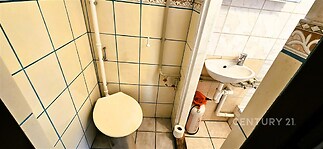 Malá koupelna s dlažbou, bílým keramickým umyvadlem a toaletou. Jednoduché obklady, klasický design, prostor pro základní hygienické potřeby.