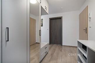 Chodba s moderními vestavěnými skříněmi, dřevěnou podlahou a světlými stěnami. Elegantní a praktické úložné prostory.