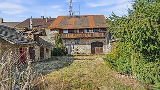 Starší dům s původními dřevěnými prvky a balkonem obklopený zahradou, vyžaduje rekonstrukci, vhodný pro milovníky venkovského bydlení.