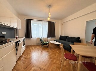 Moderní obývací pokoj s parketovou podlahou, velká okna zajišťující světlost, kombinace kuchyně a obýváku s moderním nábytkem.