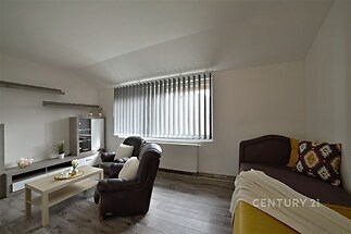 Světlý obývací pokoj s moderní dřevěnou podlahou, velkými okny a pohodlným posezením, ideální pro relaxaci a společenské chvíle.