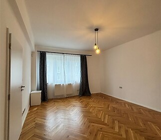 Světlý obývací pokoj s parketovou podlahou, velká okna s dlouhými závěsy, moderní osvětlení, nově rekonstruovaný minimalistický design