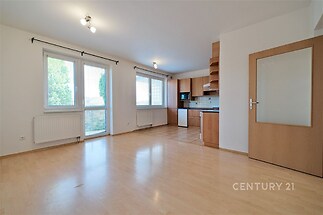 Světlý obývací pokoj s parketovou podlahou, velká okna a moderní kuchyňský kout, rekonstruovaný interiér, vstup na balkon.