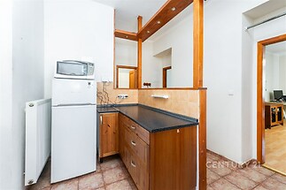 Kuchyň s dlažbou, dřevěnými skříňkami a moderními spotřebiči včetně lednice a mikrovlnné trouby, světlý interiér