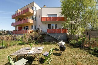 Prostorná zahrada s dřevěným posezením, moderní fasáda s balkony, klidná lokalita, vhodné pro rodinné bydlení.