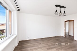 Světlý obývací pokoj s moderními svítidly, parketovou podlahou a velkými okny, ideální pro rekonstrukci nebo úpravu dle vlastního stylu.