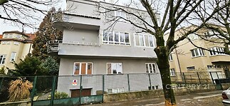 Fasáda vily s velkými okny a moderním designem, rekonstruovaný exteriér, stromy lemující ulici pro klidné okolí.