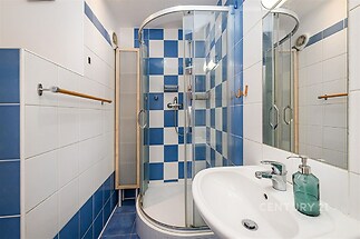 Moderní koupelna s modro-bílými dlaždicemi, sprchovým koutem a elegantním umyvadlem. Minimalistický design přidává prostor světlosti.