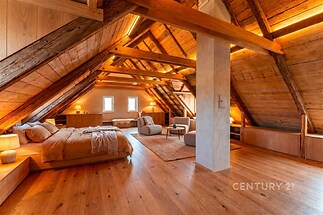 Podkrovní ložnice s parketovou podlahou, dřevěným obložením a moderním osvětlením. Útulná atmosféra s vestavěnými skříněmi a výhledem z okna.