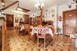 Jídelna s dlažbou, dřevěným nábytkem a rustikálním dekorem. Prostorný a světlý interiér vytváří útulnou atmosféru.