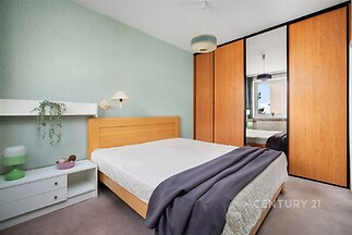 Prostorná ložnice s vestavěnými skříněmi a parketovou podlahou, moderní design a velké okno pro přirozené světlo.