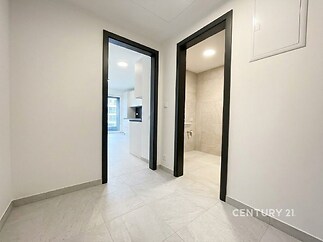 Chodba s bílou dlažbou, moderními dveřmi a přístupem do kuchyně a koupelny, světlý prostor ideální pro byt v rekonstruovaném stylu.