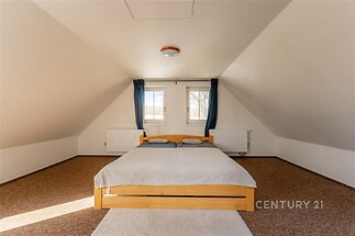 Podkrovní ložnice s dřevěnou postelí, kobercovou podlahou a velkými okny, které zajišťují dostatek světla, ideální pro moderní bydlení.