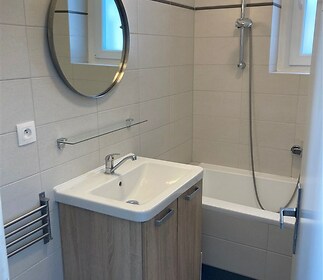Koupelna s moderními obklady, vanou a dřevěnou skříňkou pod umyvadlem, nabízí elegantní styl a praktické využití prostoru.