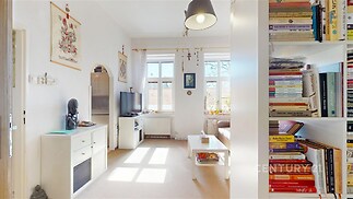 Světlý obývací pokoj s velkými okny, moderní dekorací a vestavěnými skříněmi; parketová podlaha umocňuje světlou atmosféru prostoru.