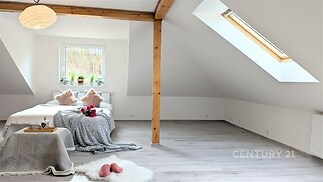 Podkrovní ložnice s velkým střešním oknem, dřevěnými trámy a světlou parketovou podlahou nabízí moderní a vzdušný prostor.