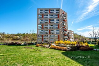 Moderní bytový dům s velkými balkony obklopený upravenou zelení a dětským hřištěm v klidné lokalitě.