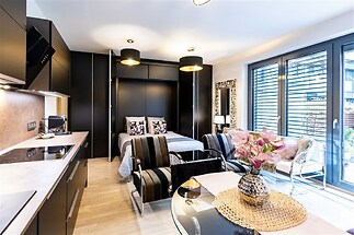 Moderní studio s parketovou podlahou, velkými okny a elegantním nábytkem nabízí komfortní a světlý prostor pro život.