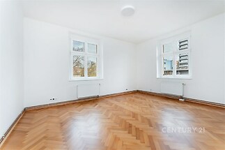 Světlý obývací pokoj s parketovou podlahou, velkými okny a moderním bílým nátěrem.