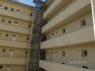 Balkony bytového domu s moderním proskleným výtahem, rekonstruovaná fasáda a úzká okna, situovaný ve městské zástavbě.