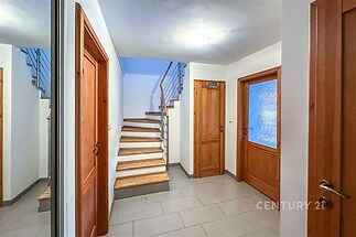 Chodba s keramickou dlažbou a dřevěným schodištěm, bílými stěnami a dveřmi z přírodního dřeva, připravena k nastěhování