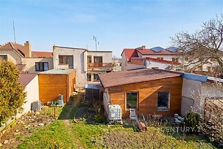 Zahrada s trávníkem a přístavbami, dřevěný zahradní domek, sousední domy. Vhodné místo pro rekonstrukci nebo rozšíření.