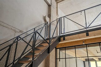 Industriální schodiště s ocelovou konstrukcí, dřevěnými schody a moderním zábradlím; betonové stěny vytvářejí stylový loftový vzhled.