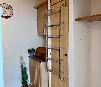 Malá kuchyň s dřevěnou parketovou podlahou, vestavěnými skříněmi a praktickým drátěným organizérem na stěně, ve světlém moderním stylu.