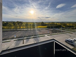 Výhled z balkonu s moderním zábradlím nabízí panoramatický pohled na krajinu a parkoviště, ideální pro milovníky přírody a klidného bydlení.