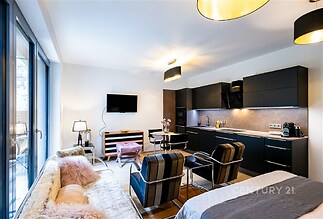 Moderní obývací pokoj s kuchyňským koutem, parketová podlaha, velká okna, elegantní černý nábytek, stylové osvětlení