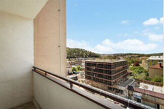 Balkon s výhledem na město a moderní budovu, ideální prosluněné místo s možností relaxace, zazděné zábradlí pro větší soukromí.