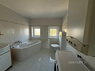 Prostorná koupelna s keramickou dlažbou, moderní vanou a dvěma okny. Světlý interiér nabízí dostatek přirozeného světla.