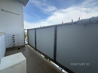 Balkon s dlažbou, poskytující dostatek prostoru pro venkovní posezení, s moderním zábradlím a výhledem na město.