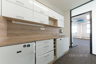 Moderní kuchyň s dřevěným obložením, bílými skříňkami a vestavěnými spotřebiči, propojená s otevřenou kancelářskou prostorou s kobercem